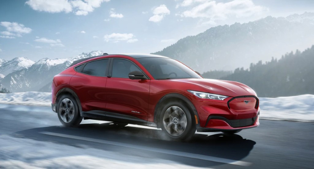 A red 2022 Ford Mustang Mach-E electric SUV is driving on the road. 