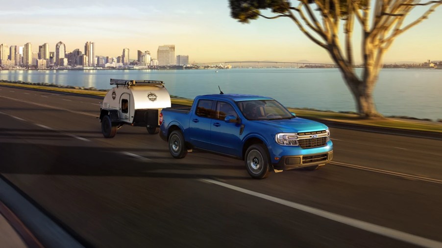 A blue 2022 Ford Maverick navigates a waterfront road in front of an urban environment.