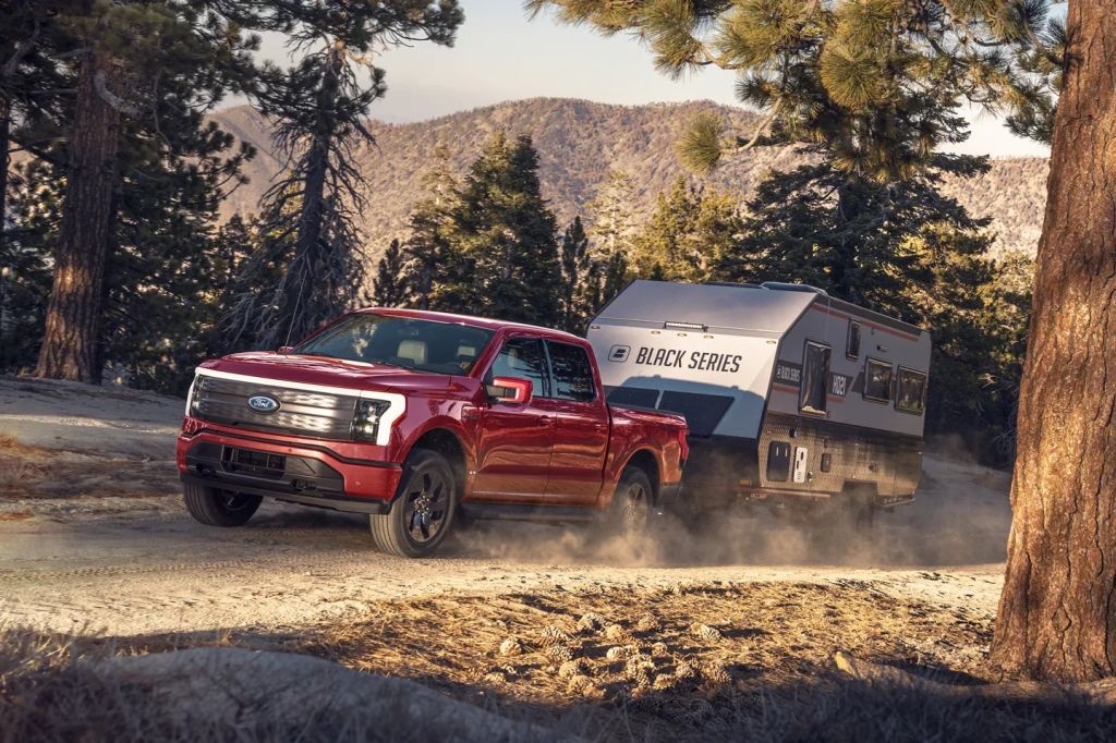 An EV Ford truck, the F-150 Lightning tows a large trailer in a mountainous terrain.