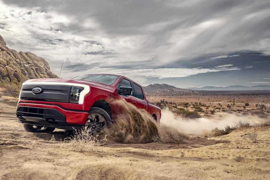 A red Ford Lightning EV truck demonstrates its capability in a desert region.