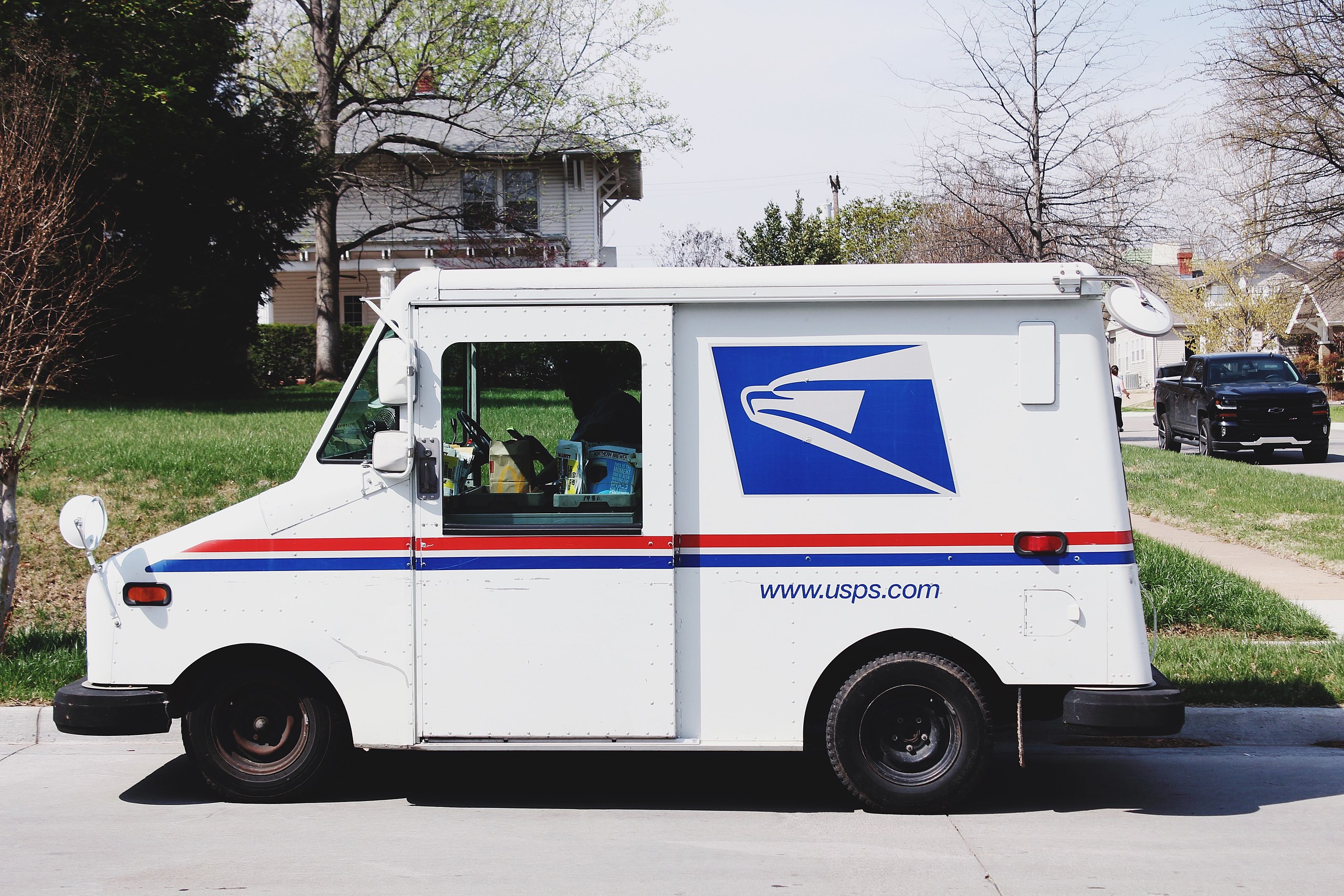 A USPS mail truck sits in a neighborhood setting.