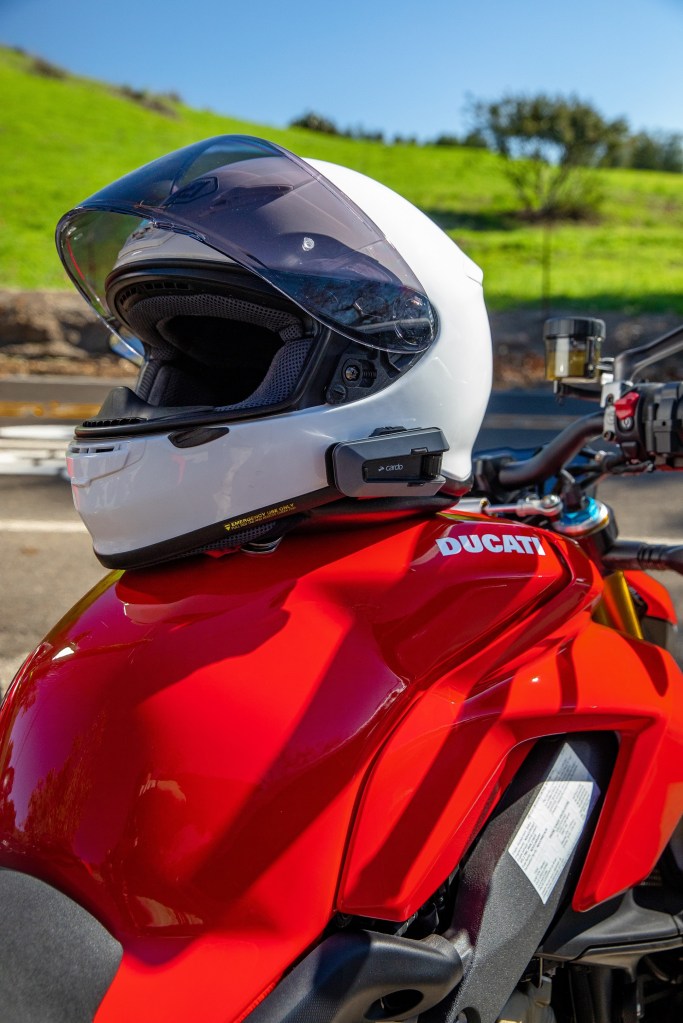 A white motorcycle helmet with a black Cardo Packtalk Edge on a red Ducati Streetfighter V4