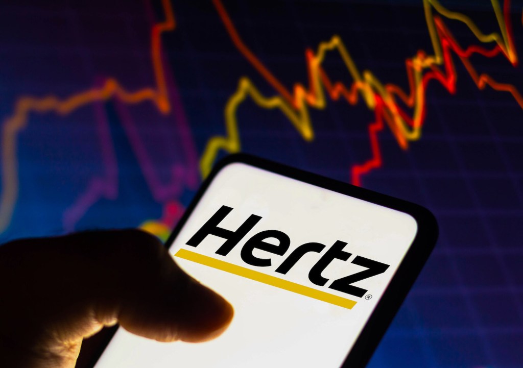 Cellphone displaying the Hertz logo in front of a stock price graph.