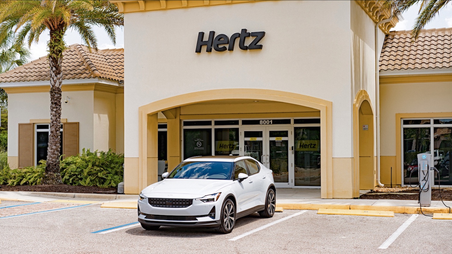 White Polestar 2 electric vehicle parked in front of a tan Hertz building.