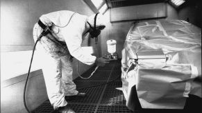 A technician in a white suit bending over the spray paint on the side of a car.