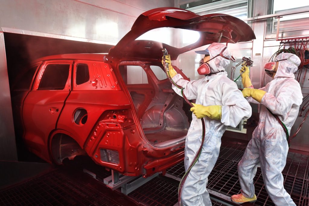 Two technicians painting a car red on a factory floor.