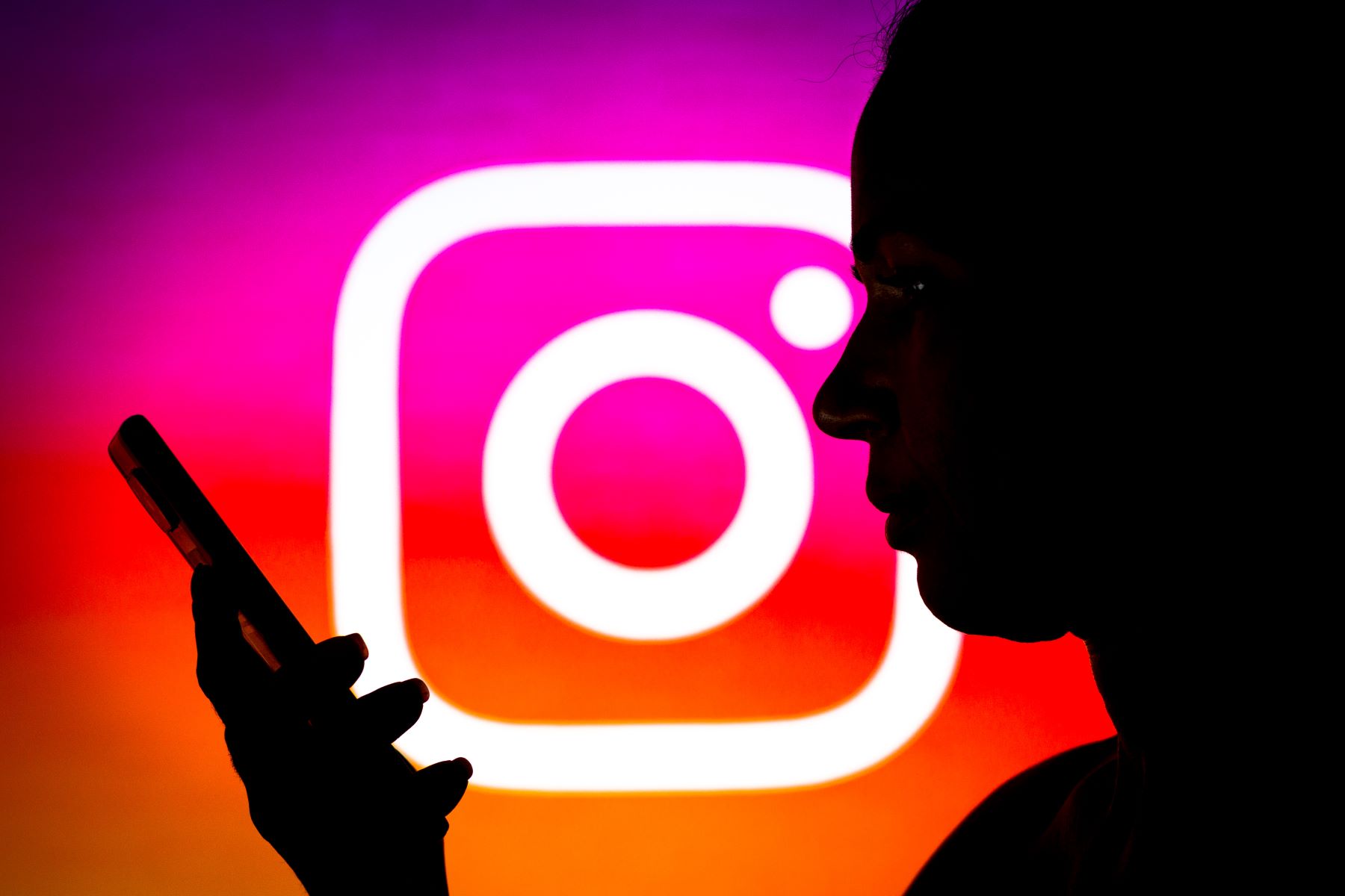 The Instagram logo behind a silhouette of a woman browsing her smartphone