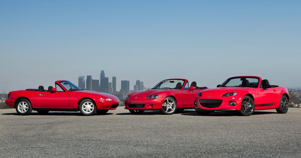 Three red Miata convertibles in front of the L.A. skyline during a Mazda car brand reunion.