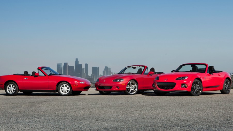 Three red Miata convertibles in front of the L.A. skyline during a Mazda car brand reunion.