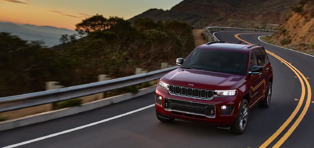 A red 2022 Jeep Grand Cherokee driving around a winding road - Goodbye Hemi V8 and Hello 4Xe plug-in hybrid power.