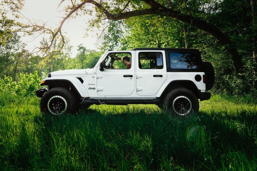 White four-door Jeep Wrangler JL Sahara parked in a field, beneath a tree.