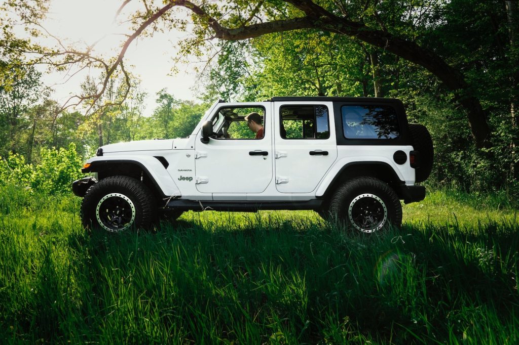 White four-door Jeep Wrangler JL Sahara parked in a field, under a tree.