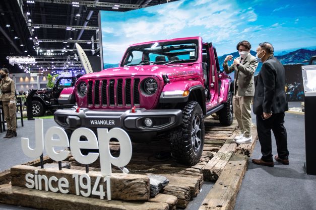 A pink Jeep Wrangler displayed with the logo printed on glass in front of it in an indoor environment with outdoor elements and background. 