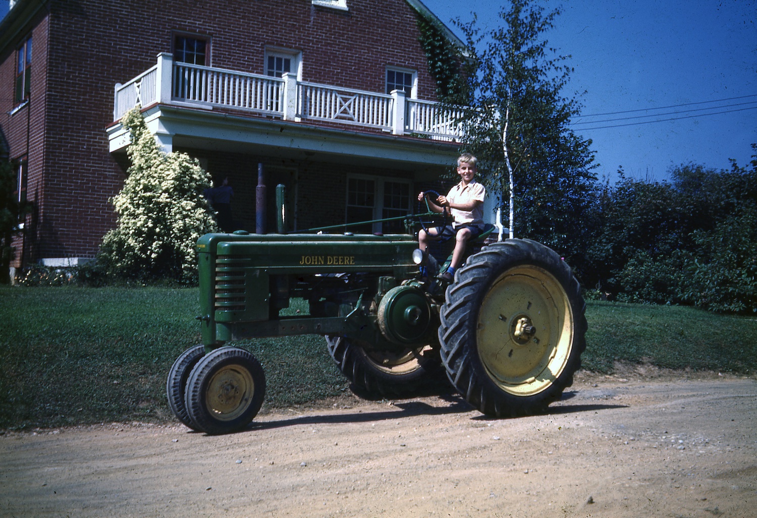 A kid drive a John Deere tractor in front of his brick house in 1946.