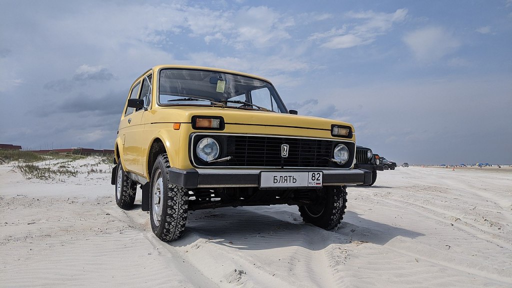A Russian 4x4 SUV, the Lada Niva sits in the sand. 