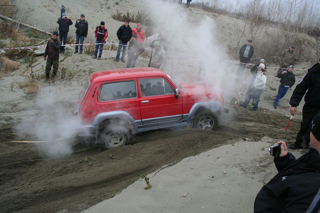 A red Lada Niva navigates a rugged dirt terrain. Showing off its capability as a 4x4 SUV.