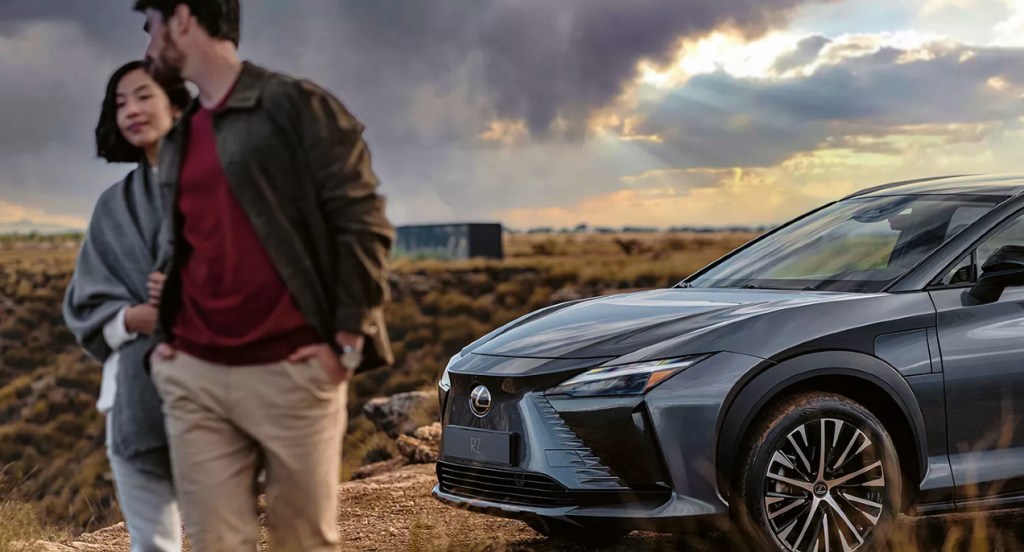 Two people stand outside near a gray 2023 Lexus 450e electric SUV. 
