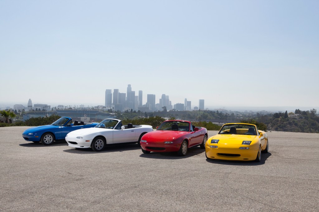 A row of Mazda Miata convertibles parked in front of the Los Angeles skyline.