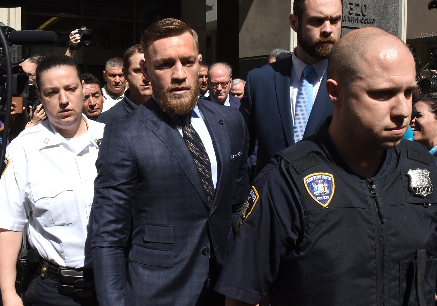 Connor McGregor wearing a suit being escorted by police to court date