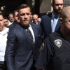 Connor McGregor wearing a suit being escorted by police to court date