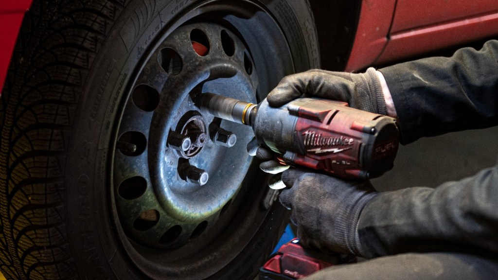a man uses a milwaukee impact driver to tighten lug nuts on a wheel