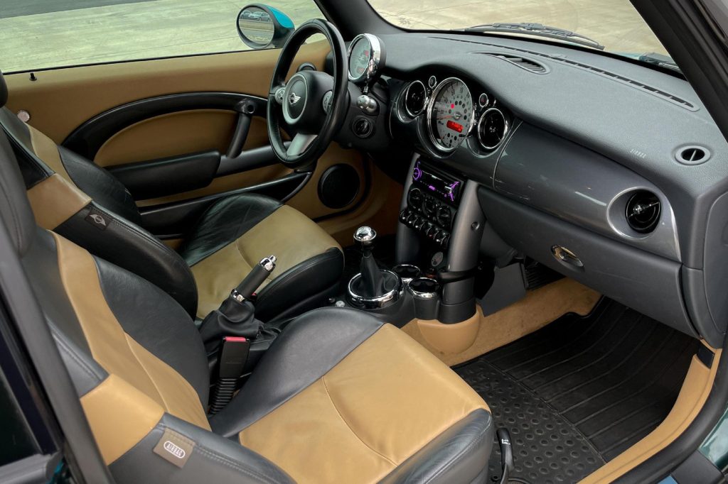 The tan-and-black-leather front sports seats and black dashboard of a modified 2005 Mini Cooper S with the JCW kit
