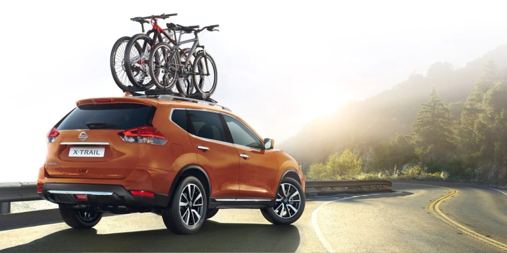 An orange 2022 Nissan X-TRAIL sits on the side of a mountain road. Using its status as an SUV to haul some bicycles. 