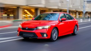 Orange-red 2022 Honda Civic driving by a large building