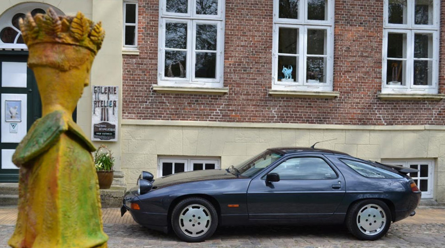 Grey Porsche 928 coupe driver's side shot in front of building