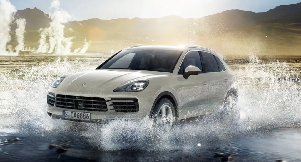 A white 2022 Porsche Cayenne E-Hybrid luxury hybrid SUV is driving through the water.