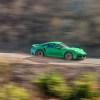 A 2022 Python Green Porsche 911 Turbo S speeds along a cliffside road during bright sunlight