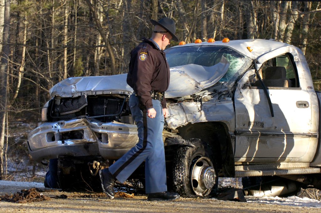 A police officer examines the wreckage of a Ram 3500 pickup truck.