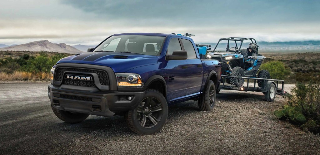 A Ram 1500 Classic Warlock wears blue paint and tows an off-road vehicle behind it.
