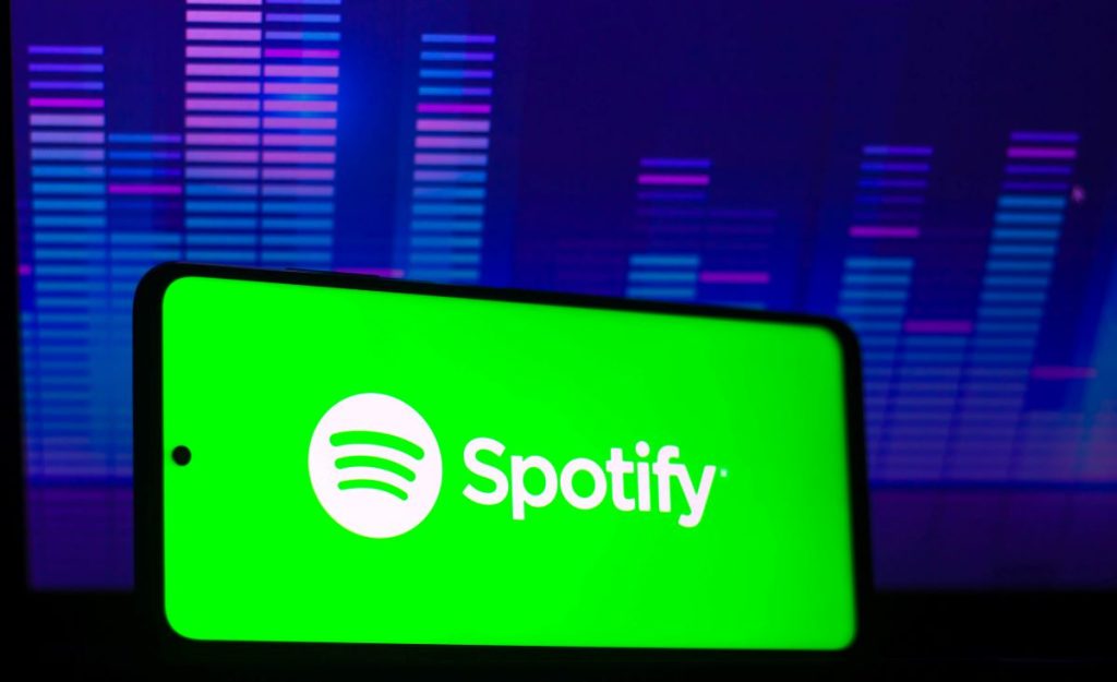 Green Spotify logo on a cell phone screen, also available in new and used cars, against a blue background. 