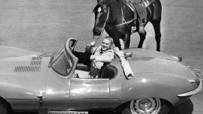 Steve McQueen in a convertible holding the reigns of a horse