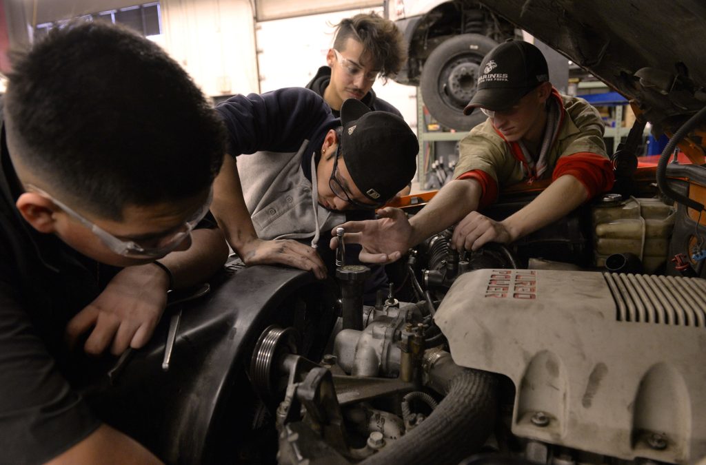 Several teenaged technical school students replace the alternator in a diesel pickup truck