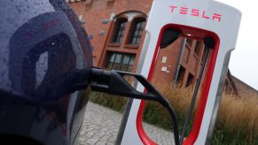 A Tesla charging at an EV charging station for Tesla with a brick building behind it.