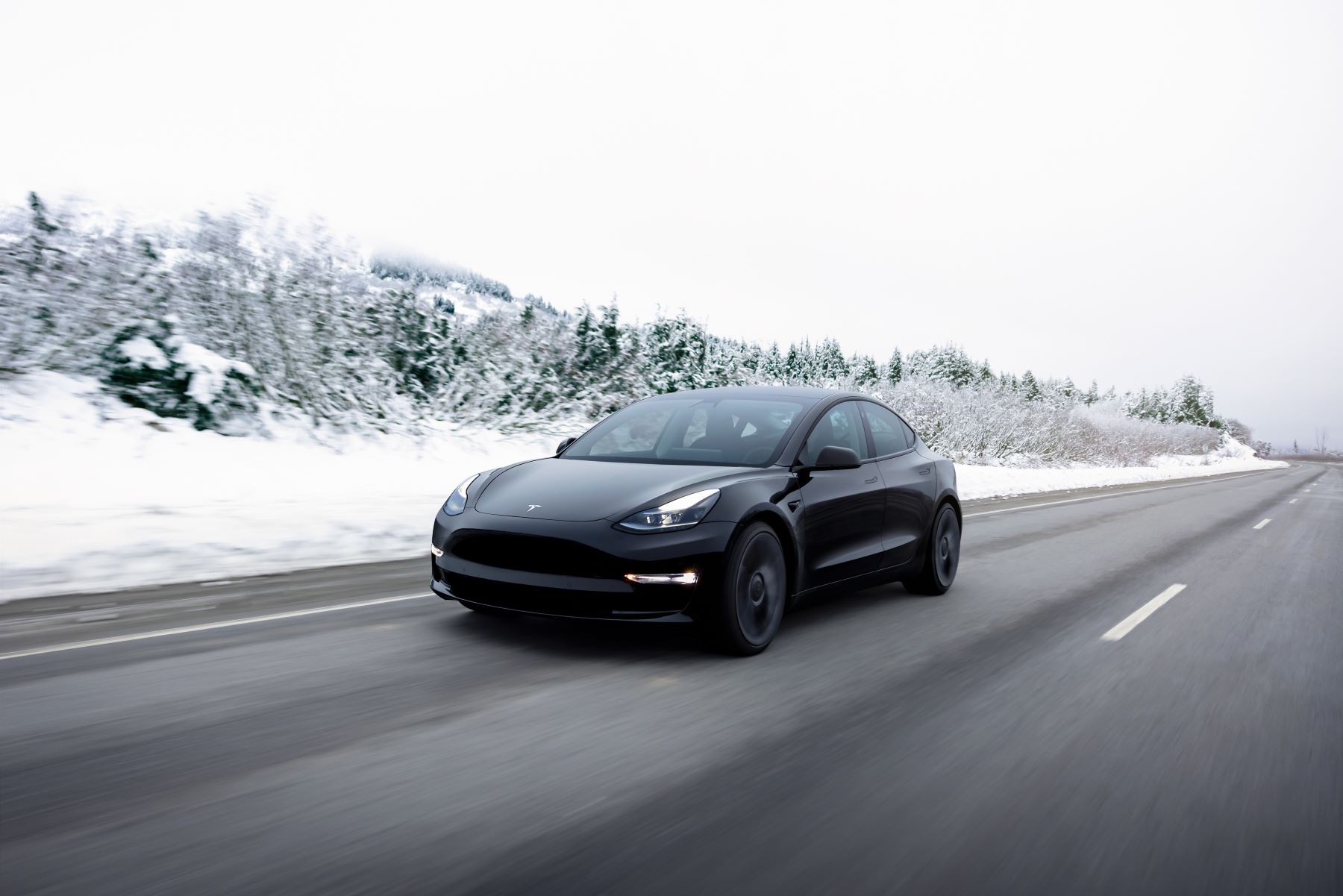The Tesla Model 3 all-electric luxury sedan driving on a highway surrounded by winter trees