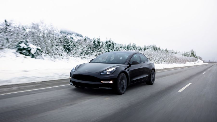 The Tesla Model 3 all-electric luxury sedan driving on a highway surrounded by winter trees