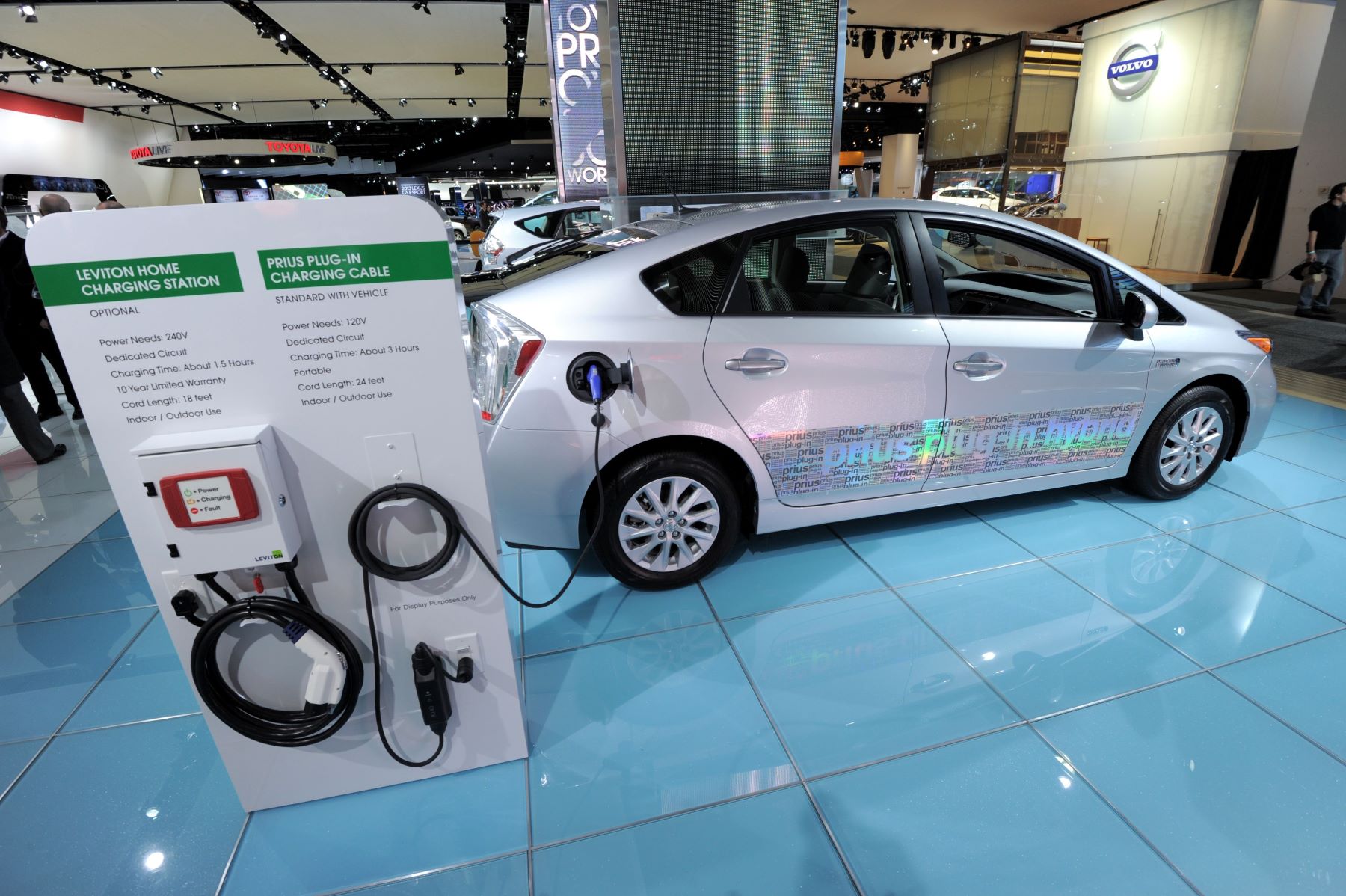 A Toyota Prius plug-in hybrid electric vehicle model on display with a home charging station and charging cable options