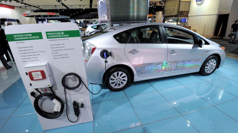 A Toyota Prius plug-in hybrid electric vehicle model on display with a home charging station and charging cable options