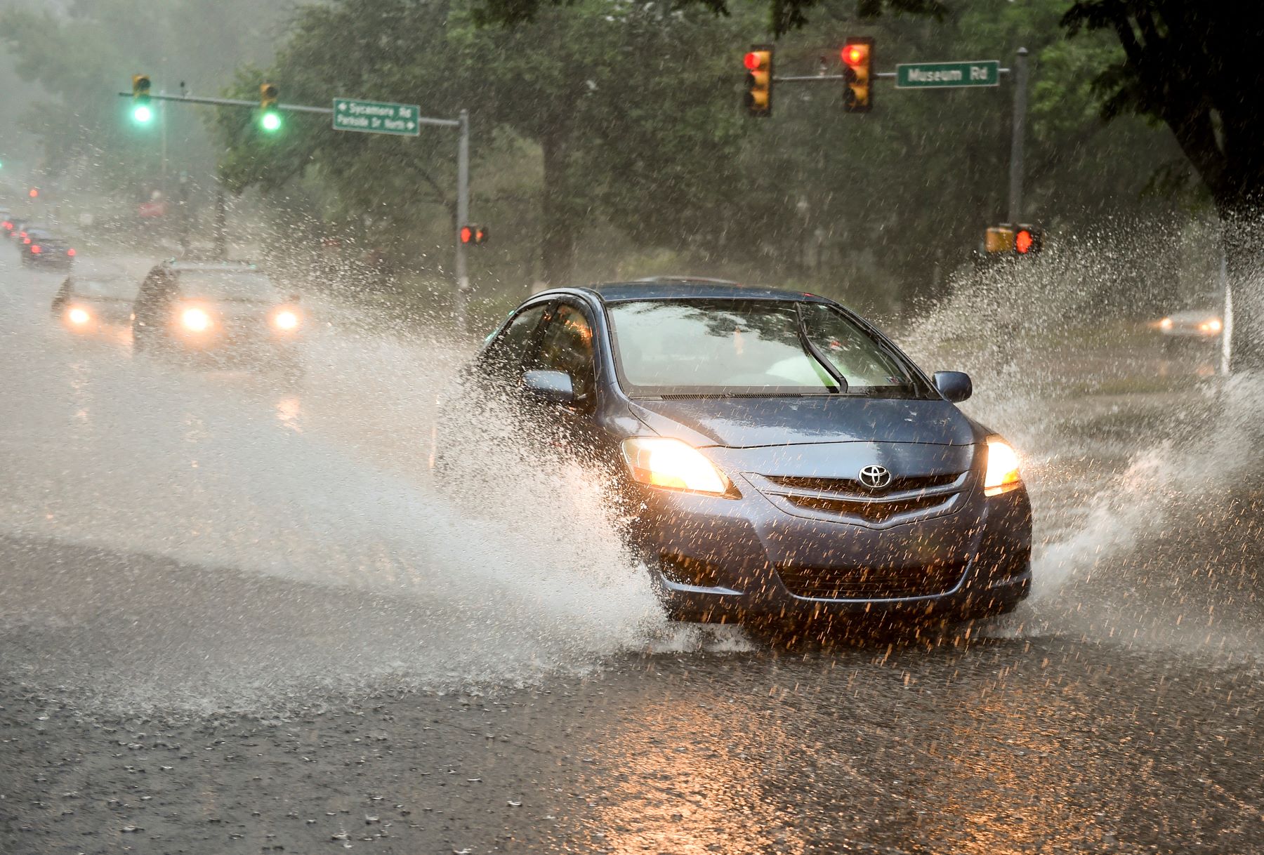 A blue Toyota car driving through rain puddles with its headlights on