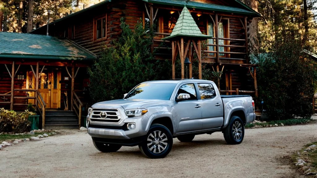 A mid-size Toyota Tacoma sits outside of a log house, showing the styling of the SR5 trim.