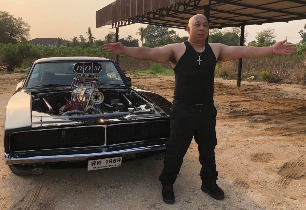 Looks like Vin Diesel in Thailand standing in front of a Fast and Furious Dodge Charger