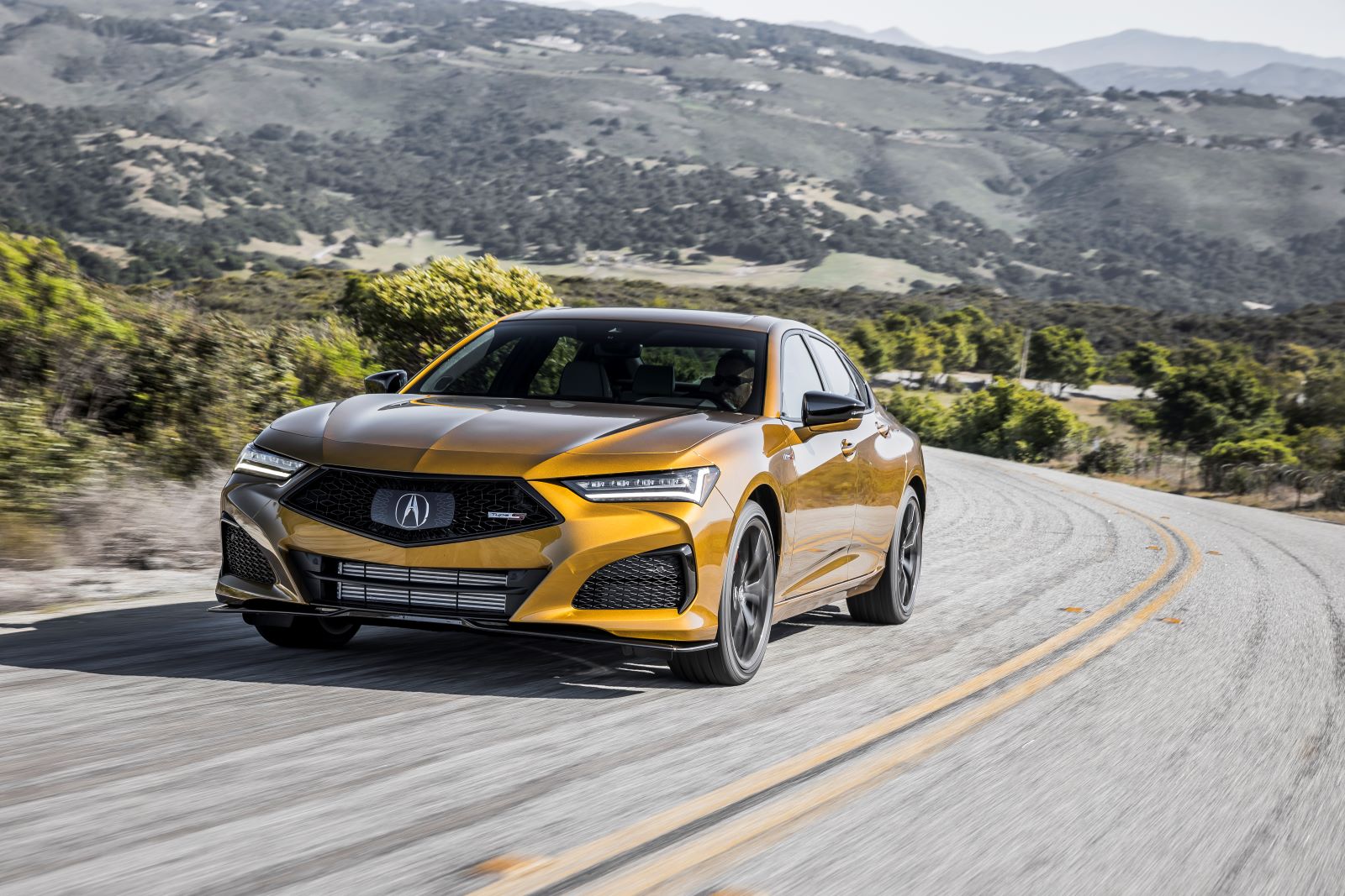 Golden-yellow Acura TLX, a reliable used luxury car, tearing up a winding road in the mountains