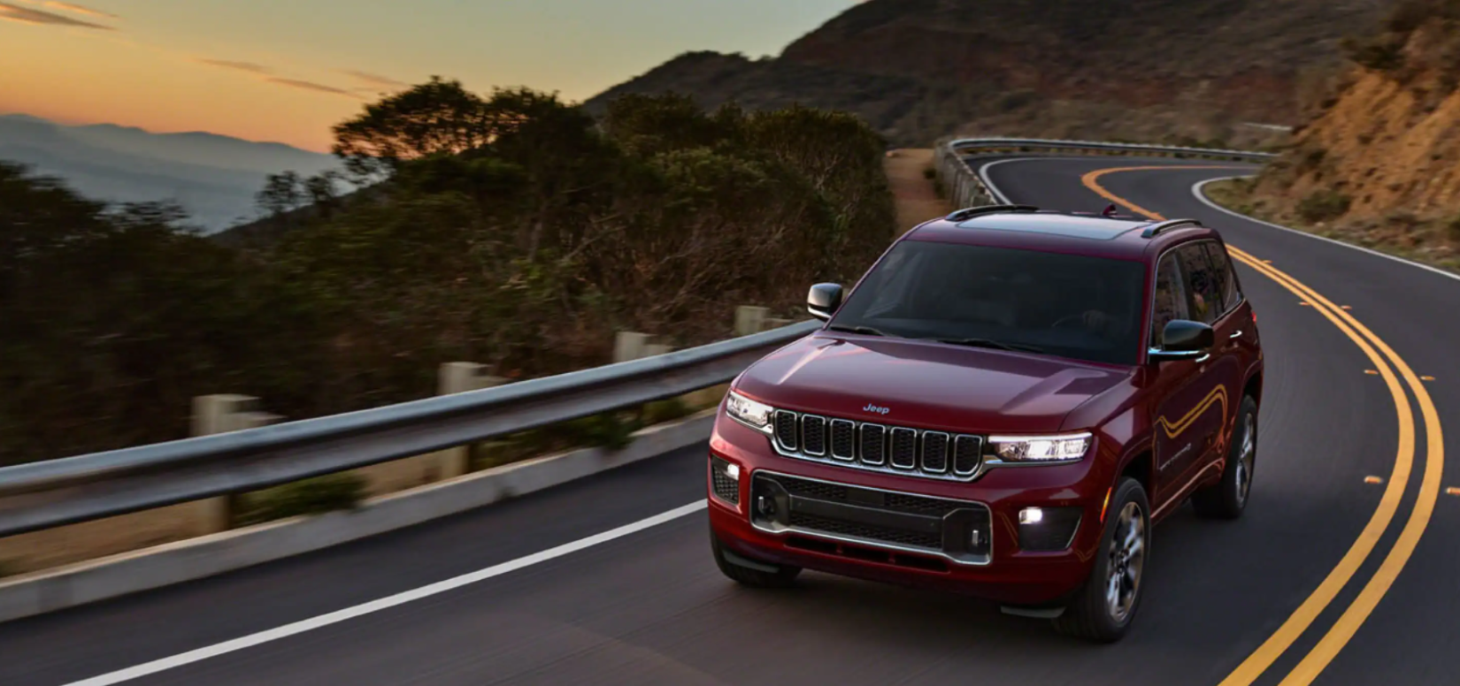 The all-new 2022 Jeep Grand Cherokee midsize SUV in dark red driving down a twisting coastal highway
