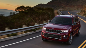 The all-new 2022 Jeep Grand Cherokee midsize SUV in dark red driving down a twisting coastal highway