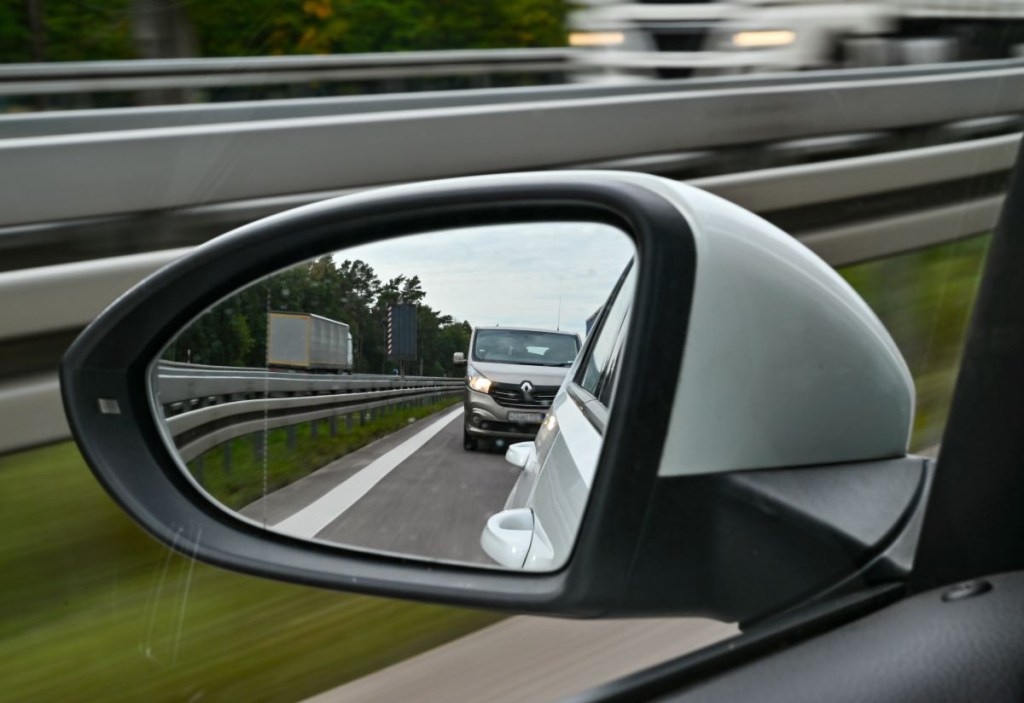 A large grey van is shown in the side-view mirror of a car traveling on the highway