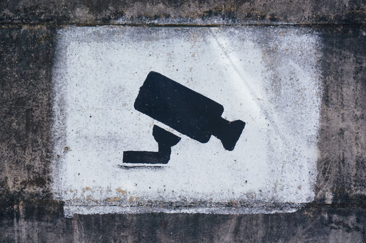 A spraypainted sign, black surveillance camera icon over a white rectangle painted onto a concrete wall