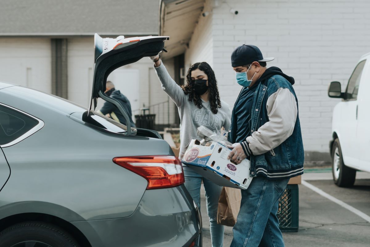 Folks loading a box of groceries into a sedan's open trunk area
